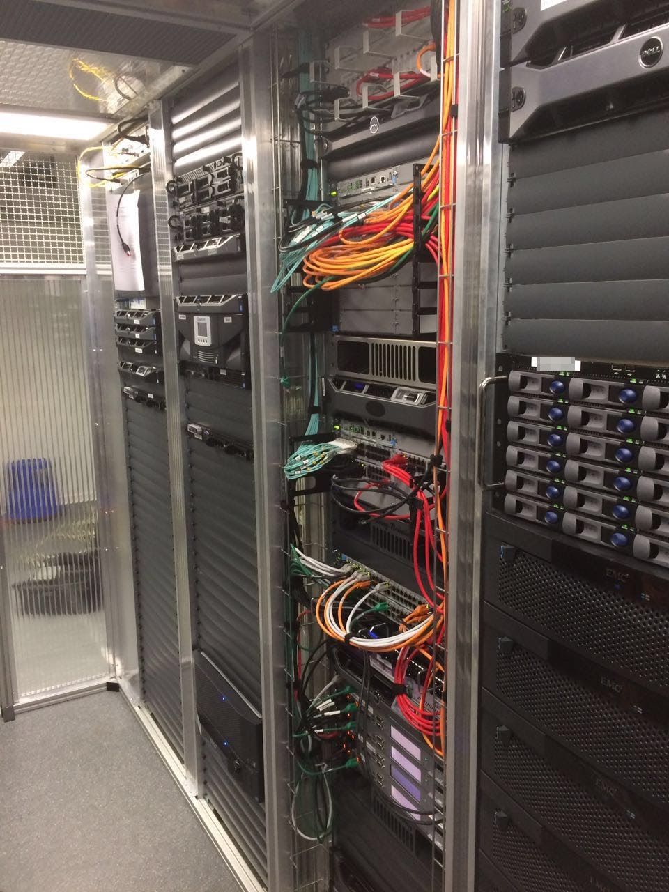 Gang zwischen zwei Serverschränken mit Rackservern und Speichersystemen, davor gebündelte Datenkabel.